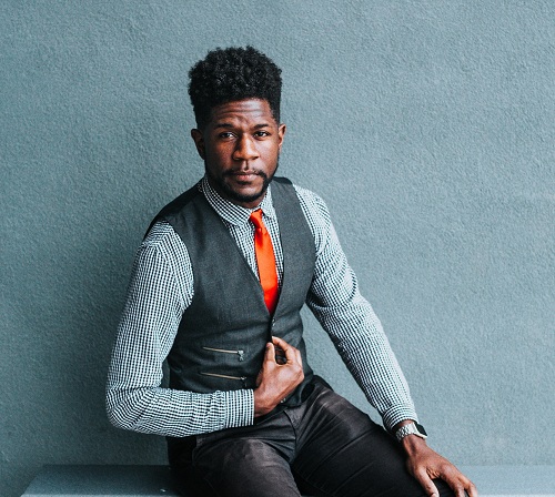 Dark man in Orange tie and grey jacket posing for camera